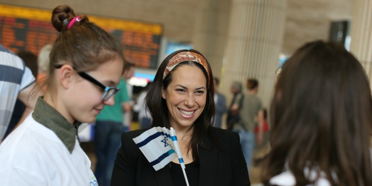 Yael Eckstein holding a small flag of Israel while smiling and chatting with Jewish youth