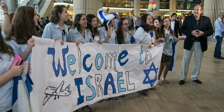Girls holding a white Welcome to Israel banner with Rabbi Yechiel to the right.