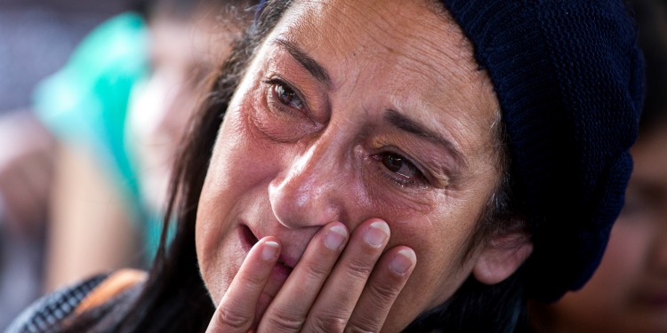 A middle-aged Jewish woman looking to her left as she wipes tears from her face.