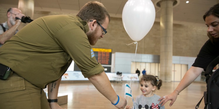 A soldier shaking the hand of a young girl who's holding a balloon.