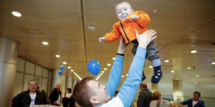 Father happily tossing newborn son into the air after making Aliyah
