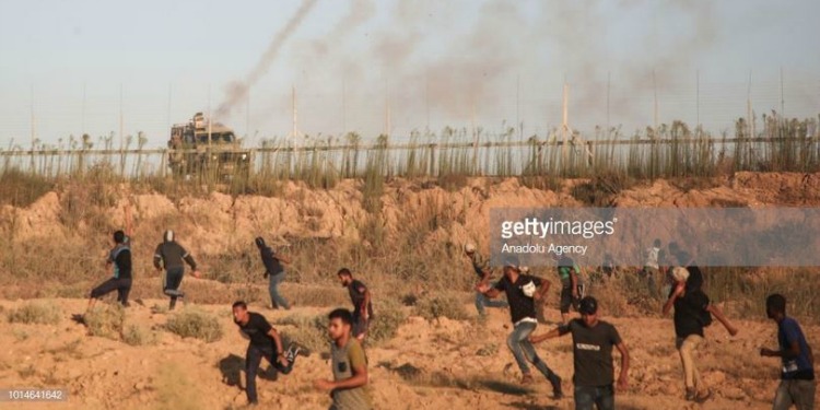 Several people running away from a fence in a sandy terrain.