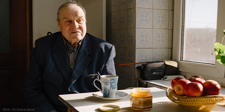 Elderly man sit at table by window with teacup, honey, and apples