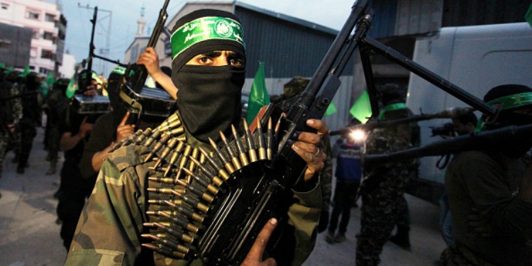 A soldier in a black mask holding an armed weapon with ammo strapped around him.