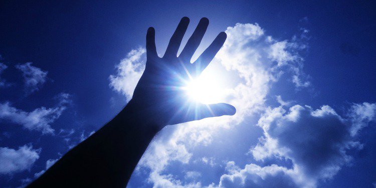 Picture of a hand reaching up with a cloudy blue sky behind it.