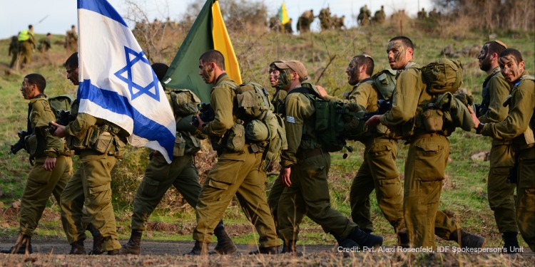 The Golani Brigade waving two flags in the air as they march on a hill.