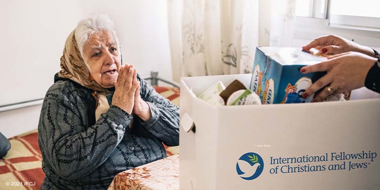 Elderly Jewish woman praying in gratitude while receiving IFCJ food box.