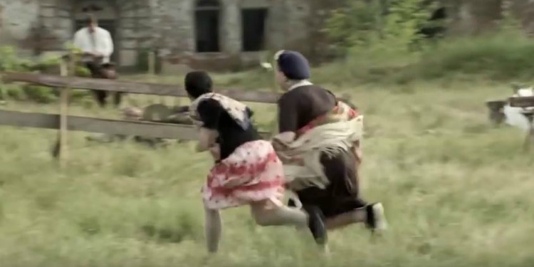 Two women running in a field with a wooden fence.