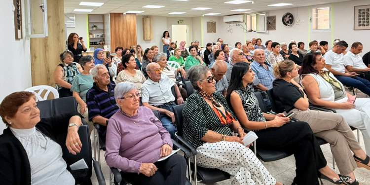 A diverse group of elderly individuals seated in a community hall, attentively listening during a meeting or presentation.