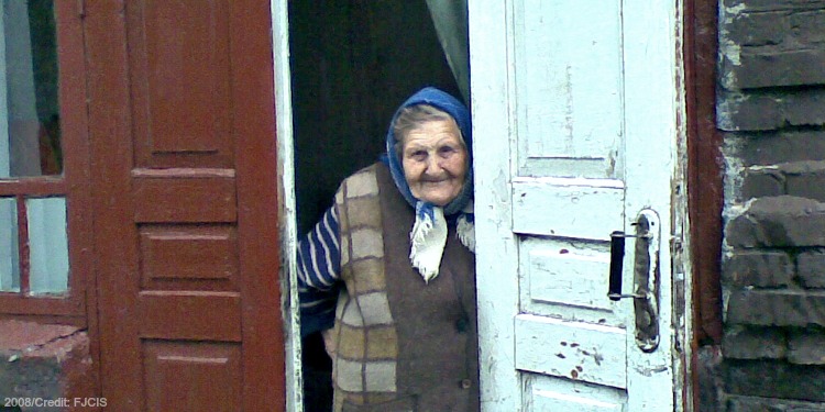 Elderly Jewish woman in winter clothing exiting a red and white door.