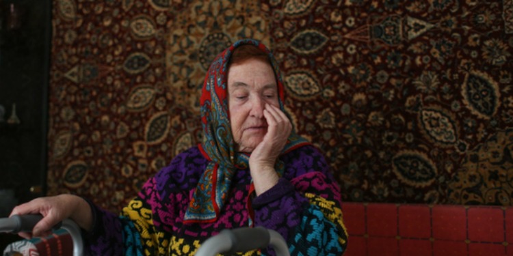 Older Jewish woman sitting on couch while holding on to cane hoping for relief