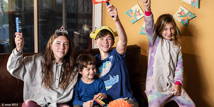 Yael Eckstein's children dressed up for Purim as their smiling holding up a toy on their couch.