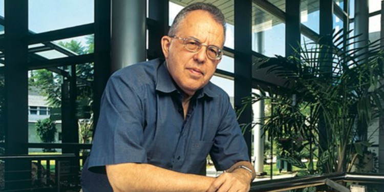 Israeli Haim Harari, with his arms folded over a balcony in an all-glass building with greenery.