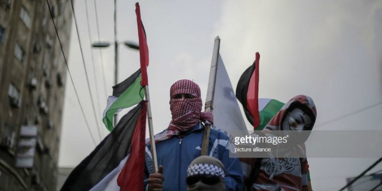 Three men wrapped in head scarfs waving flags.