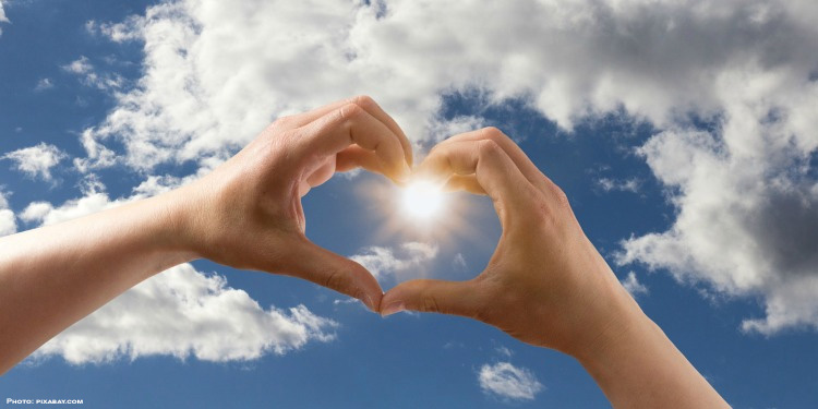Hands in a heart shape against a cloudy blue sky.