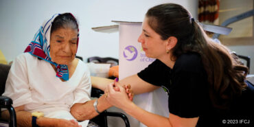 Elderly Jewish woman sitting with and talking to a Fellowship worker.