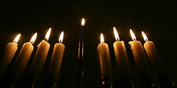 Close up image of candles lit for Hanukkah against a black background.