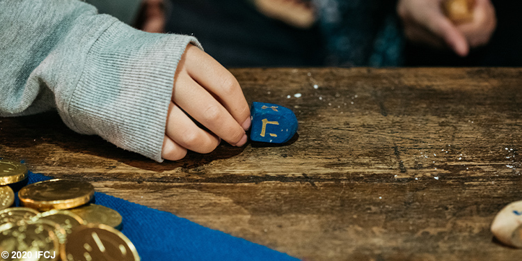 A person holding a dreidel against a wooden table.