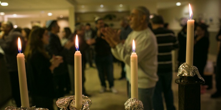 Four candles lit during Hanukkah while people behind the candles are dancing.