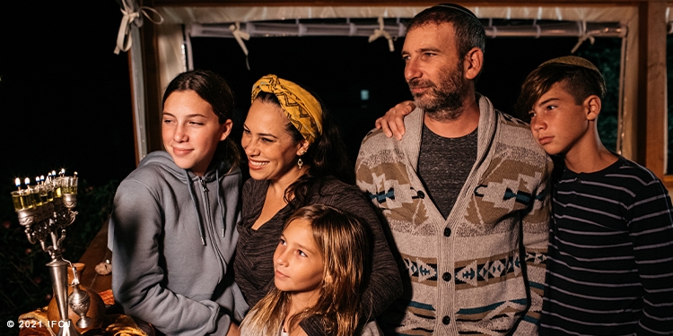 Yael and her family standing in front of Hanukkah candles