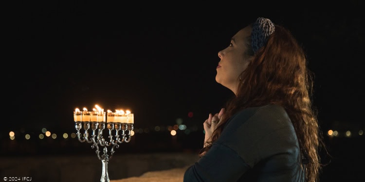 Yael Eckstein, dark green shirt, blue headscarf, Hanukkah, menorah, hands together, looking up, praying