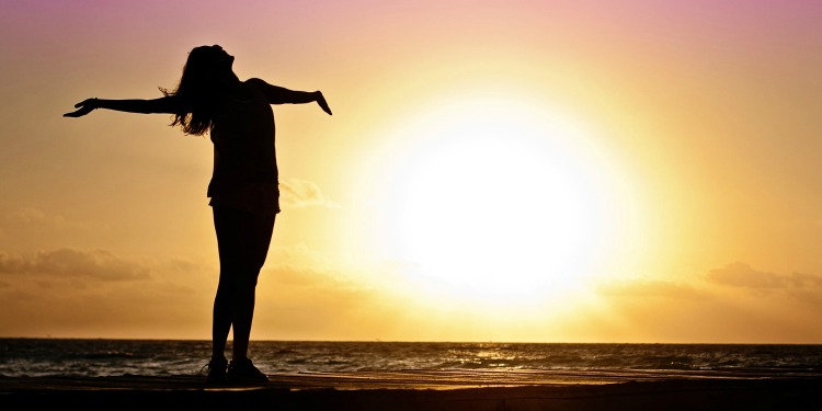 Woman having her hands stretched out against the sunrise.