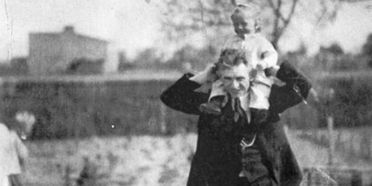 Black and white image of a man with a young girl on his shoulders.