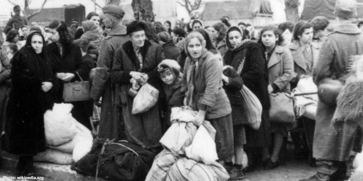 Black and white image of Jewish people during the Holocaust holding bags looking into the distance.