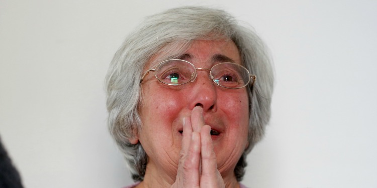 Elderly Jewish woman holding her hands in prayer while crying.