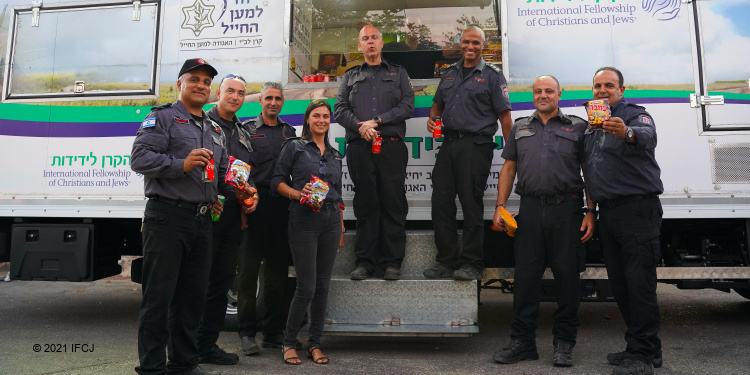 Workers in front of an IFCJ food truck holding snacks.