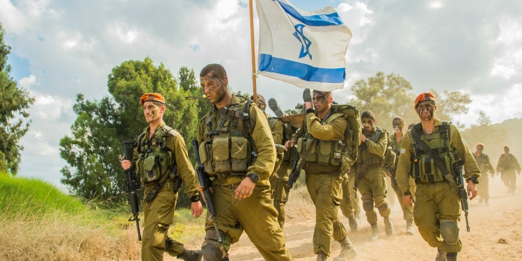 IDF soldiers holding an Israeli flag while working on a dirt road.