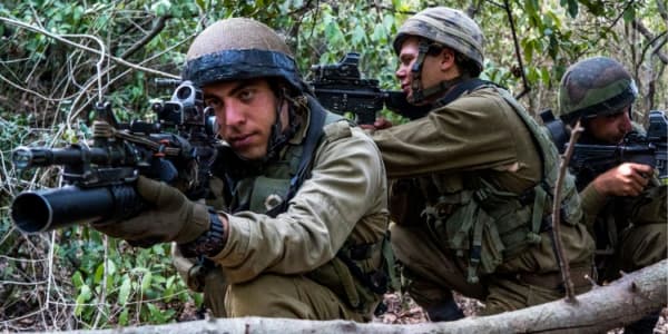 Three IDF soldiers in a ready position in the middle of the forest.