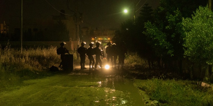 Several men with gas masks walking the street at night.