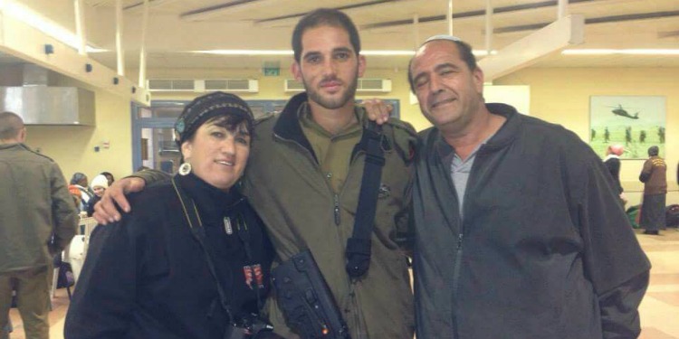 An IDF soldier standing with two civilians embracing them.