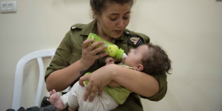 A female soldier bottle feeding a small baby that's in her arms.