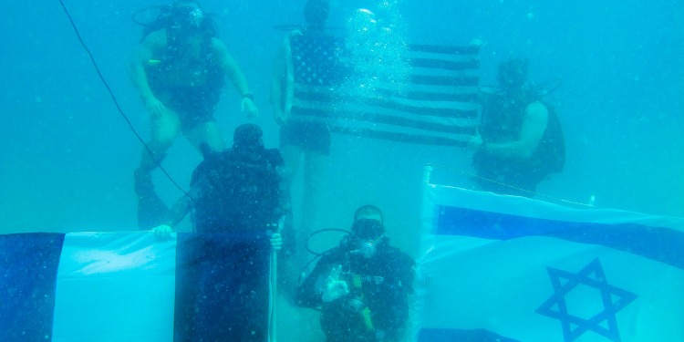 Five IDF divers in full gear holding up three flags.