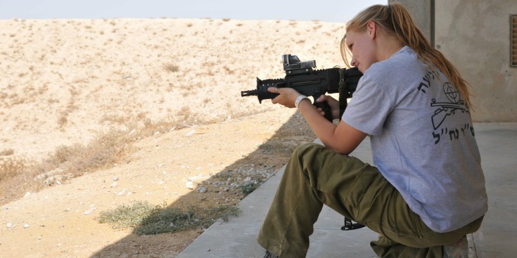 An IDF soldier holding a gun in a ready position during a field training exercise.