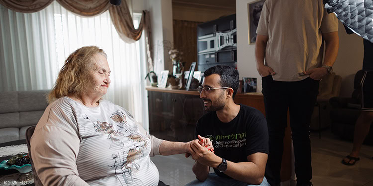 IFCJ employee assisting an elderly woman in a chair
