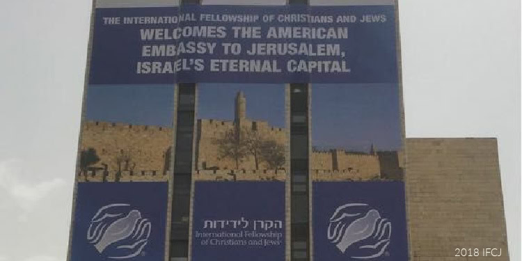 Sign welcoming visitors to the American Embassy in Jerusalem, Israel's eternal capital, with a background of historic walls and blue sky.