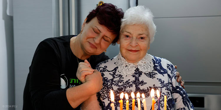 IFCJ staff with elderly woman holding hands in fron of hanukkah candles