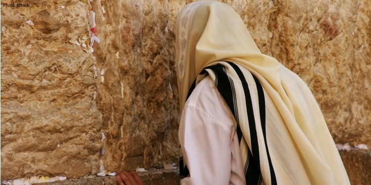 Man in a white robe praying at the Western Wall.