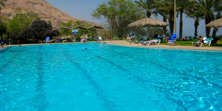 A pool with lounge chairs and trees around it.