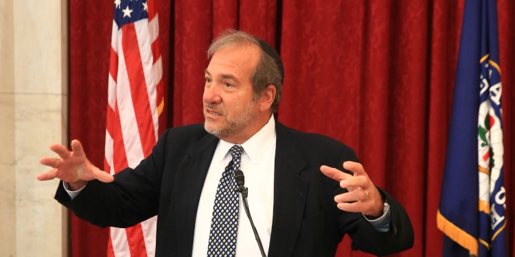 Rabbi Eckstein standing at a podium with two flags behind him.