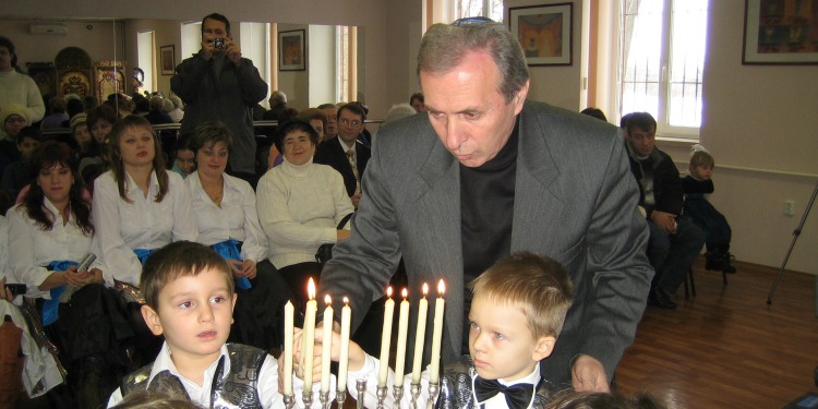 Man helping small children light the menorah during Hanukkah.