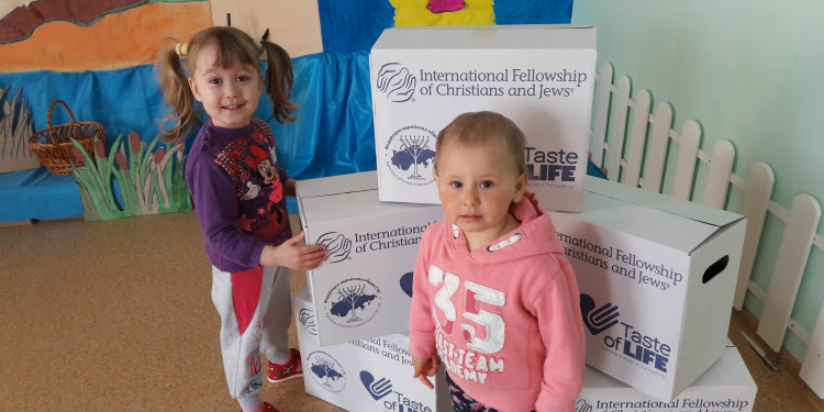 Two young girls with several IFCJ branded food boxes behind them.