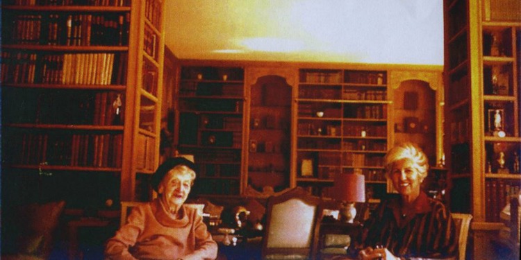Dated image of two women sitting together in a room full of books.