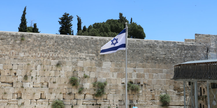 The Israeli flag waving in front of a brick wall.