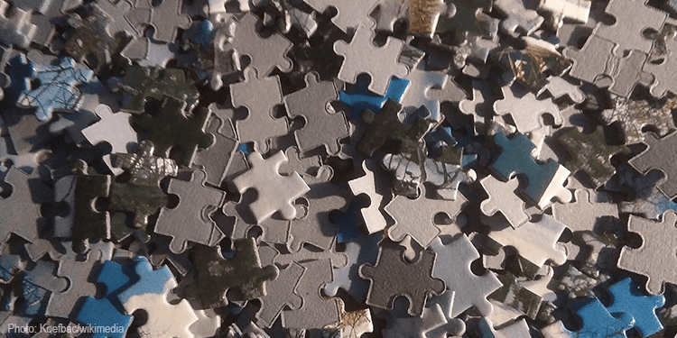 Close-up of scattered puzzle pieces in various shades of gray, blue, and green, symbolizing connection and unity.