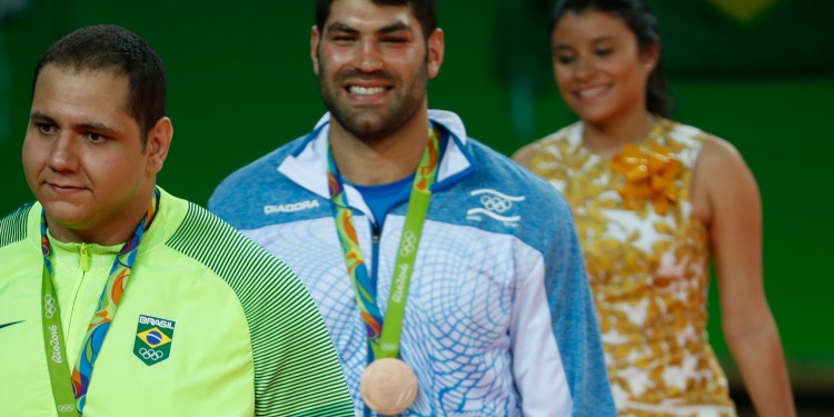 Three people walking in a single line while two of them have medals around their necks for the 2016 Olympics.