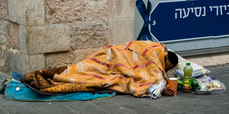 A man sleeping on the street with a meal in an aluminum tin and juice next to him.